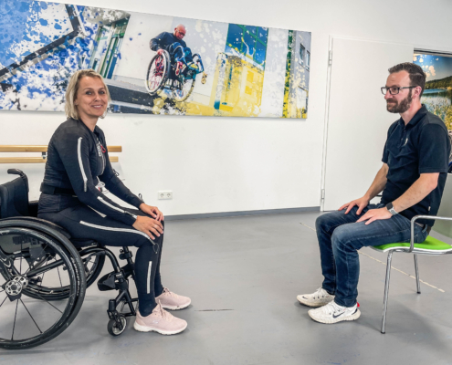 Patientin sitzt im Rollstuhl, gegenüber sitzt ein rahm Mitarbeiter